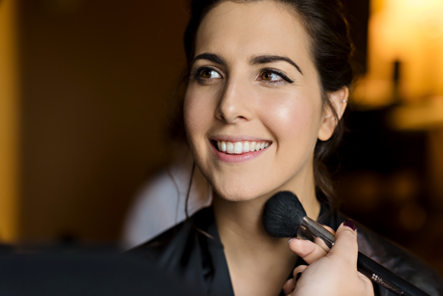 A bride smiles as her makeup artist finishes her makeup.